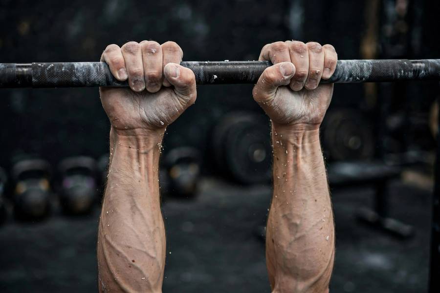 Close-up of chalked hands gripping a pull-up bar in a dead hang