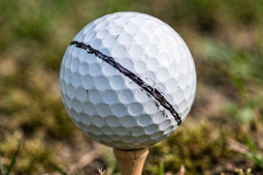 Photorealistic close-up of a golf ball marked with a Sharpie line on a tee, shallow depth of field