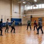 Basic Rules of Volleyball for Beginners (Explained) Beginners playing volleyball on an indoor court with a net dividing the two teams