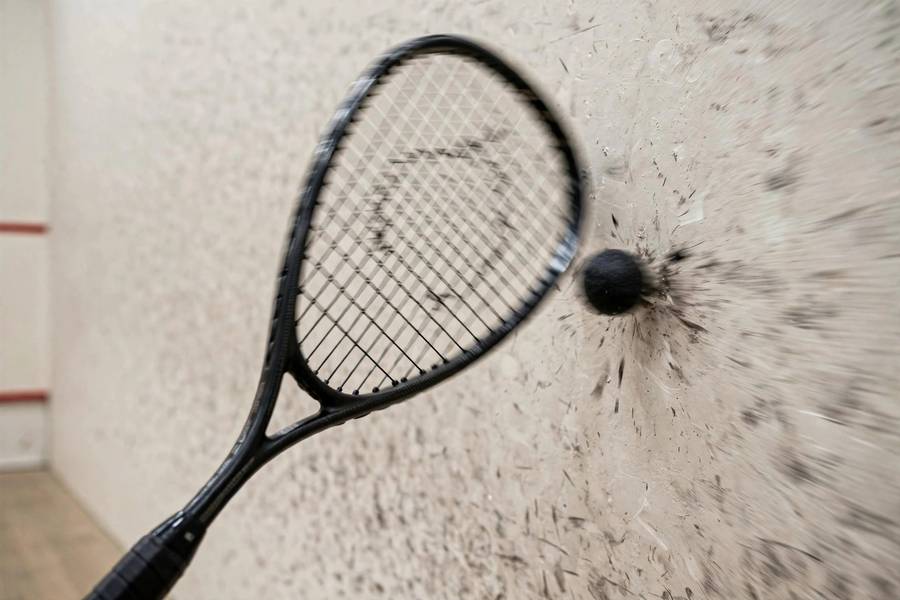 Photorealistic close-up of a squash racket striking a small black ball against the front wall, motion blur