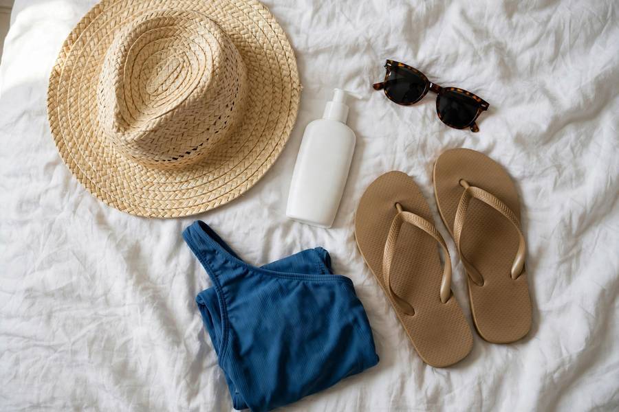 A flat-lay of beach vacation packing list essentials — hat, sunscreen, and light clothing