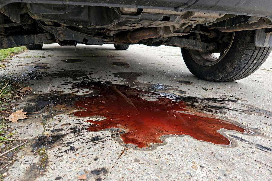 Red transmission fluid puddle leaking under a parked car in a driveway