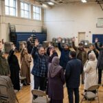 Caucus vs Primary Difference: How Each System Works Voters gathered in a school gymnasium participating in a caucus meeting with raised hands