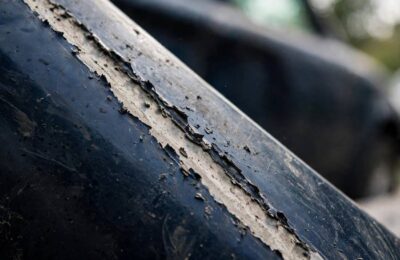Close-up of a deep car scratch showing primer through the paint — do car scratches rust