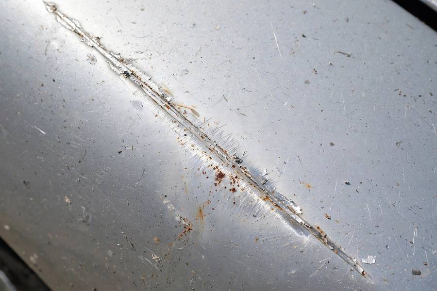 Early rust forming along an untreated scratch on a car fender