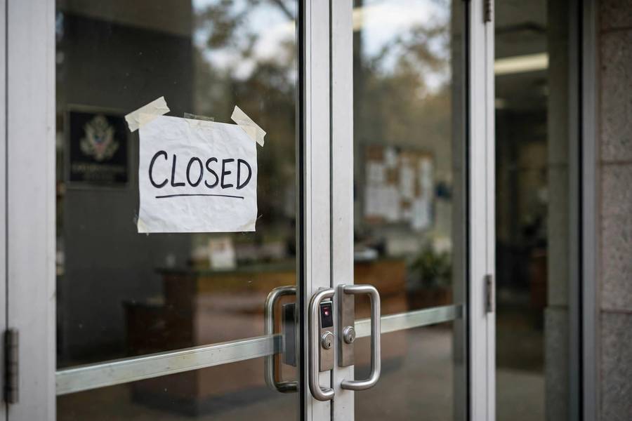 A closed sign hanging on the locked entrance doors of a federal government building