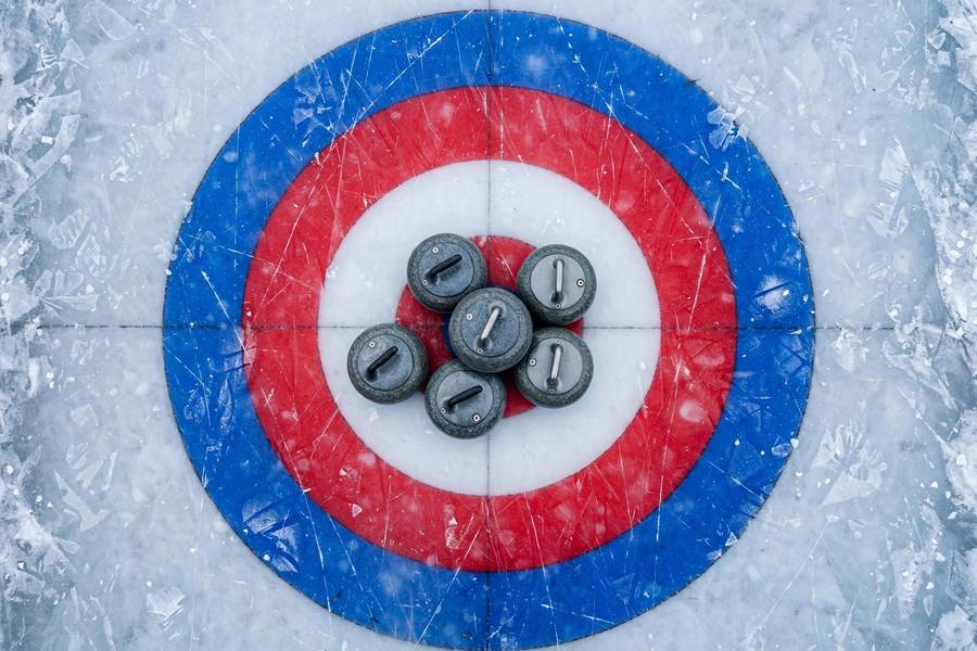 Curling stones clustered around the house target on the ice