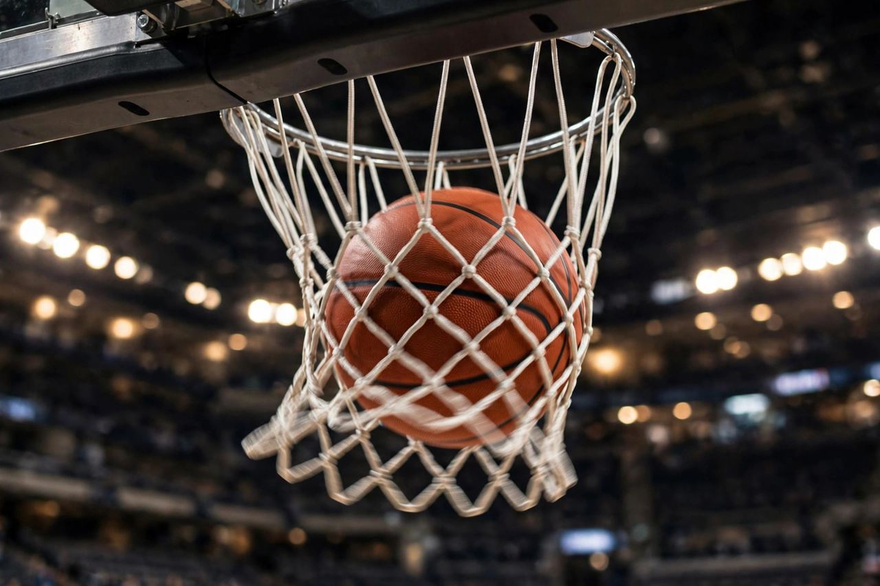Close-up of a basketball going through a hoop with arena lights