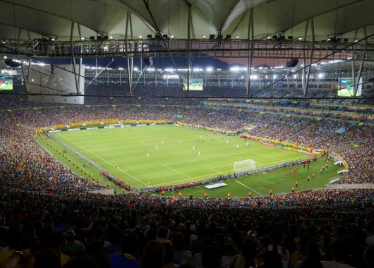 A packed soccer stadium glowing under floodlights during a night match