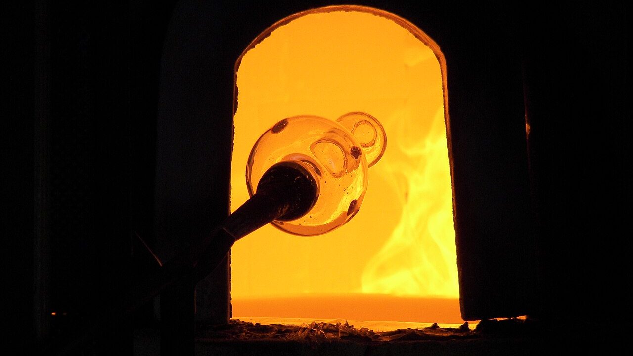 Molten glass on a blowpipe being reheated inside a glowing glassblowing furnace