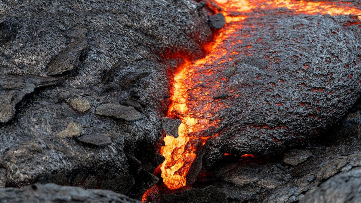 Close-up of bright yellow-orange lava glowing through a crack in dark, cooling lava rock