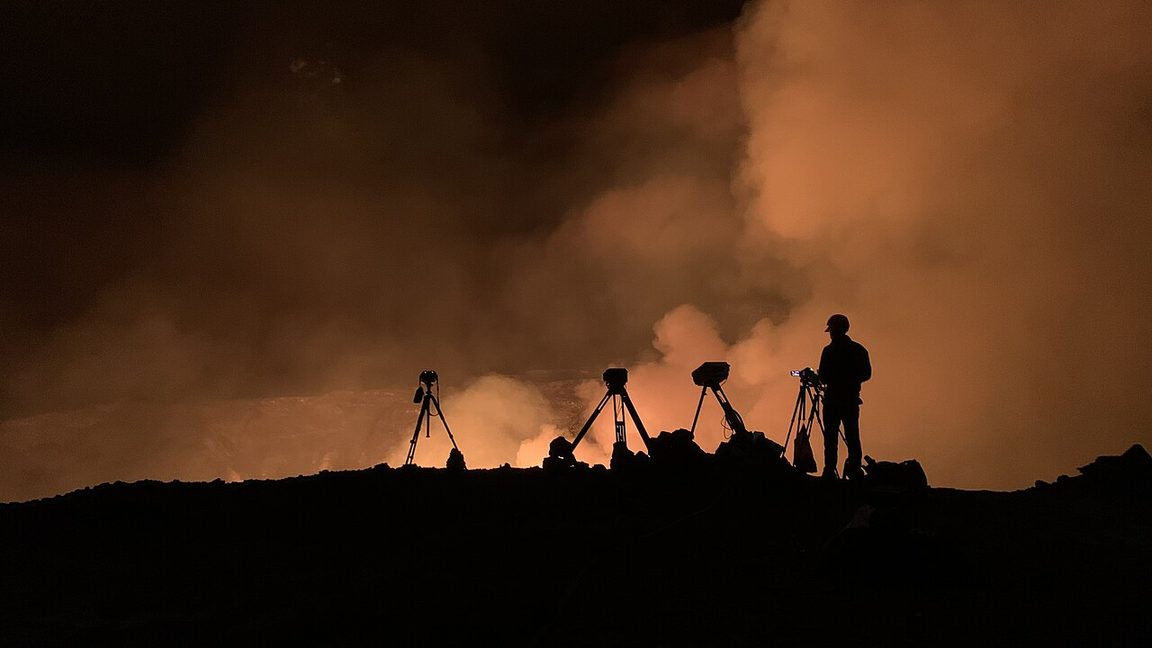 A USGS scientist silhouetted beside monitoring instruments at the rim of Kilauea's crater at night