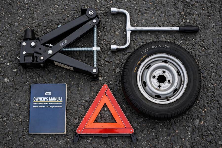 Essential tools laid out for how to change a tire: jack, wrench, spare, and warning triangle