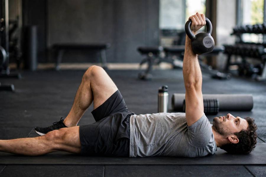 Man in the starting floor position of a Turkish get-up pressing a kettlebell toward the ceiling