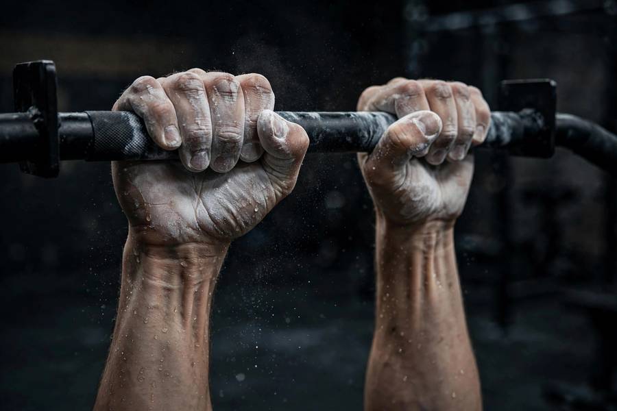 Close-up of chalked hands gripping a pull-up bar with determination