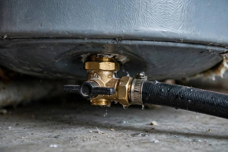 Close-up of a water heater drain valve with a hose connection at the bottom of the tank
