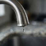 How to Fix a Leaky Faucet (A 30-Minute DIY Repair) Kitchen faucet close-up with a single water drop