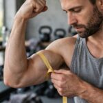 How to Get Bigger Arms: The Coach's 6-Rule Blueprint Man measuring his bicep growth with a tape measure