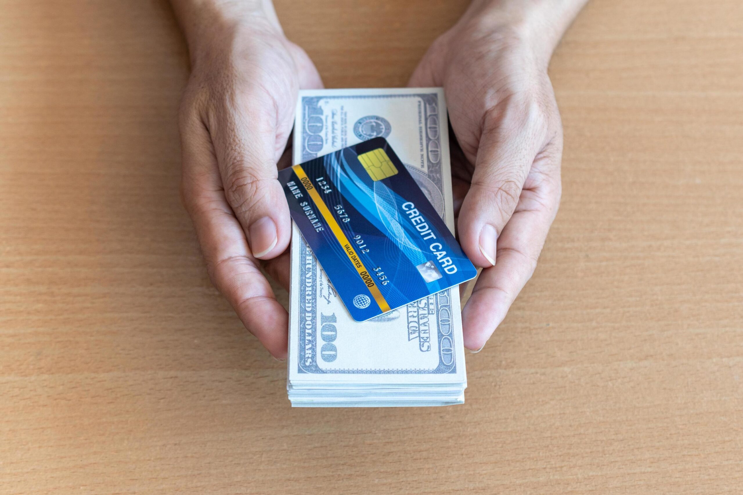 Hand holding a credit card above a stack of monthly bills on a table