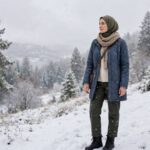 How to Layer Clothes for Winter Without Looking Bulky Woman in a stylish winter coat with scarf standing in falling snow