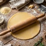 How to Make Homemade Pasta Without a Machine Fresh homemade pasta dough being rolled flat with a rolling pin
