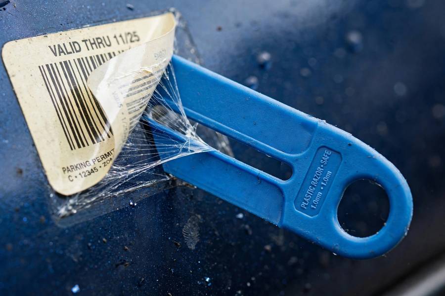 Plastic razor blade lifting a sticker edge, the safe tool for how to remove stickers from car surfaces