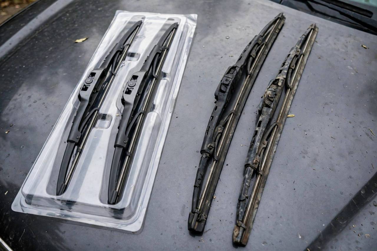 New windshield wiper blades in packaging next to old worn blades on a car hood