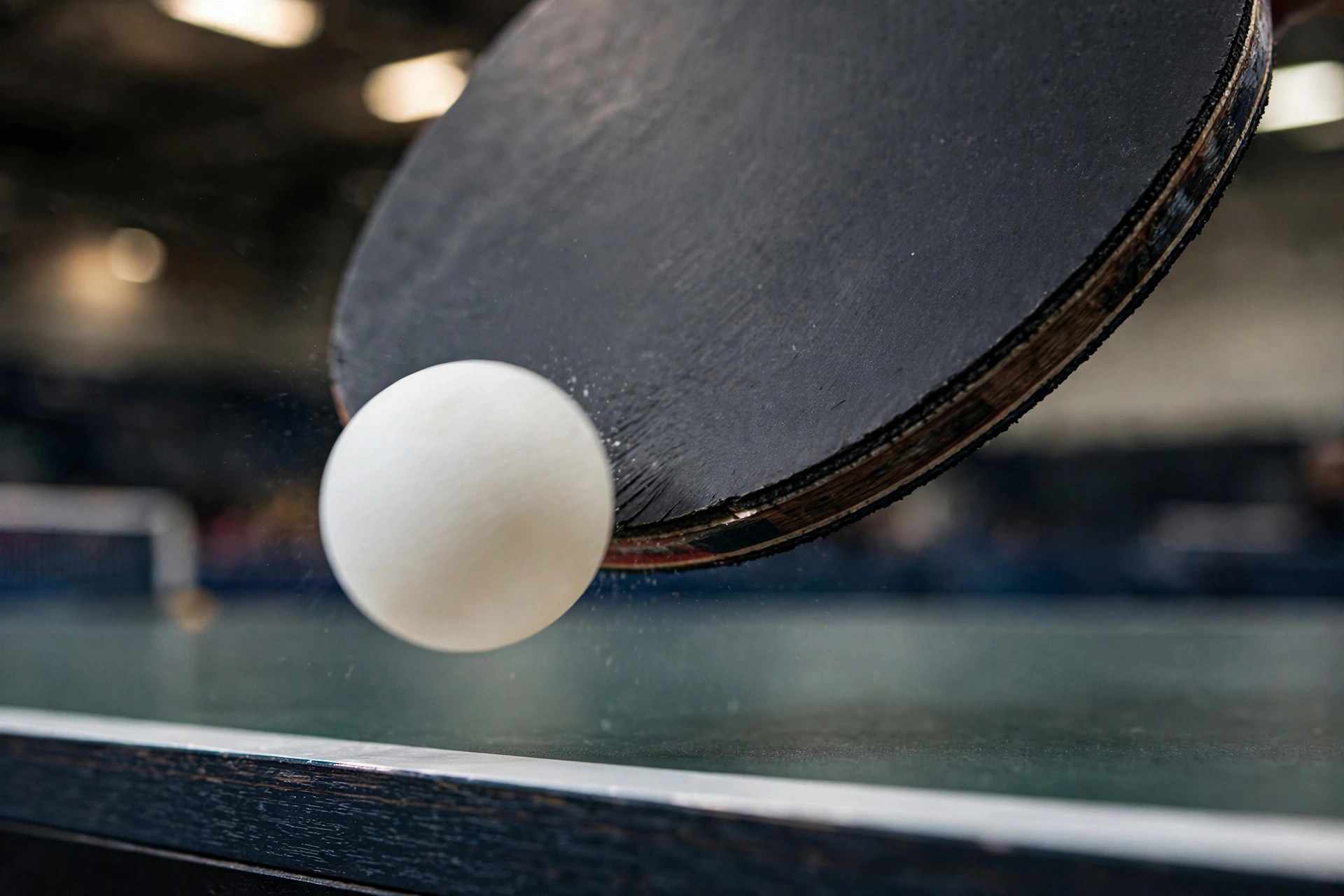 Close-up of a paddle striking the ball during a table tennis serve, showing brushing contact