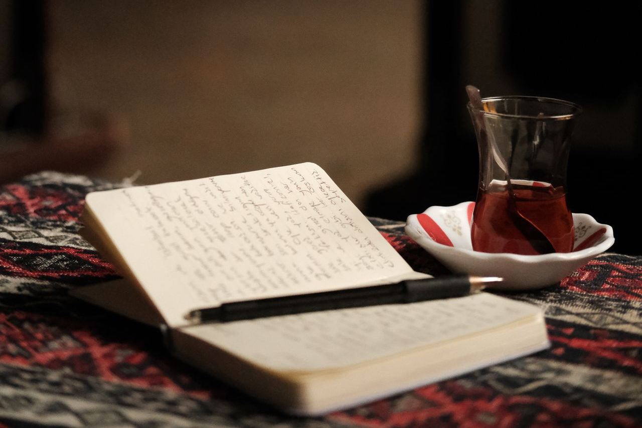 Open journal with handwritten entries beside a cup of tea on a wooden desk