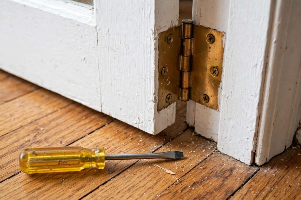 Close-up of an interior door hinge with a screwdriver beside it