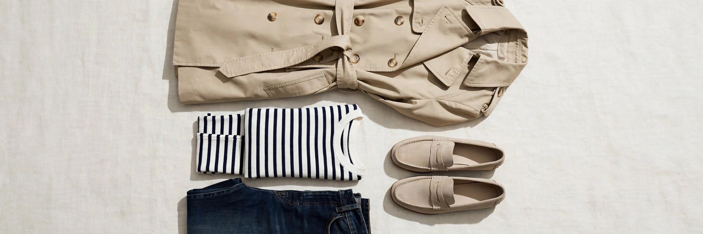 Flat lay of trench coat styling essentials: beige trench, striped top, dark jeans and loafers arranged together