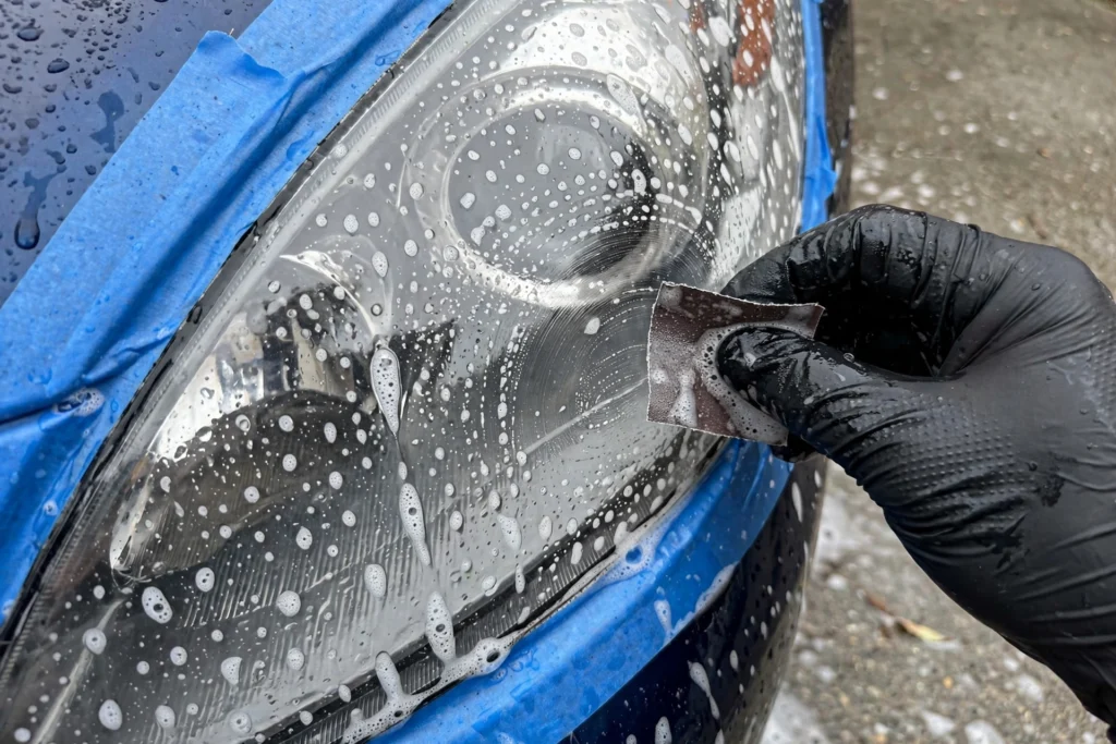 Wet-sanding a cloudy headlight with fine-grit sandpaper during restoration
