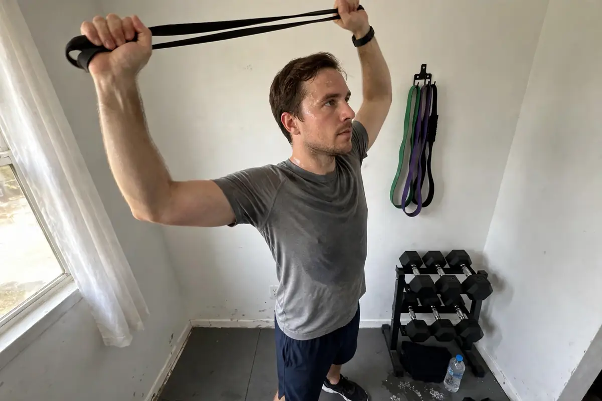 Man using a resistance band for an overhead shoulder stretch in a home gym