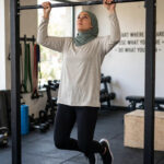 Pull-Up Progression for Beginners: From Zero to Your First Rep Beginner woman practicing scapular pull-ups while hanging from a bar