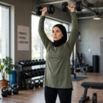 8 Best Shoulder Exercises for Women (Toned, Defined, Not Bulky) Woman performing dumbbell overhead press in a gym