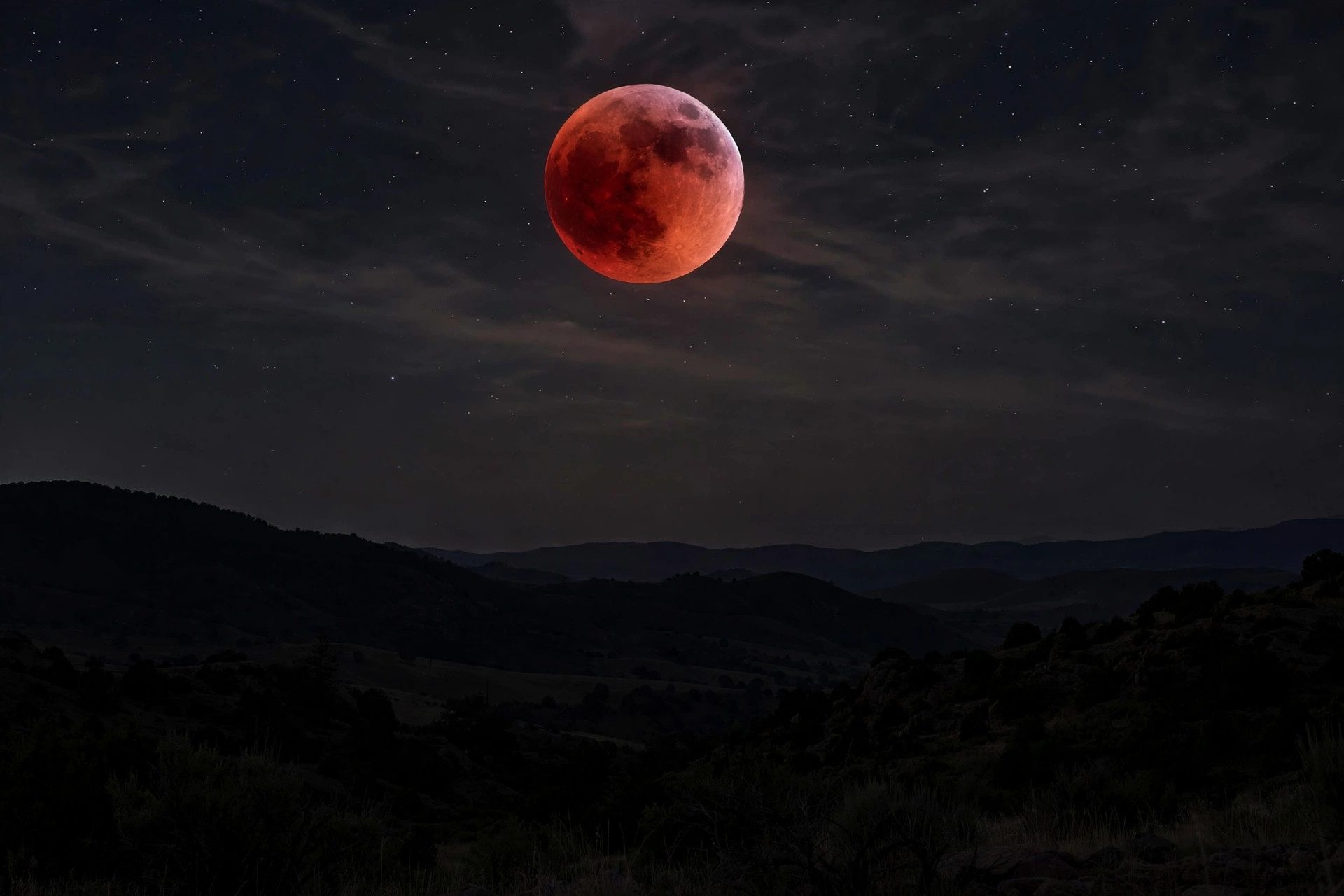 Reddish lunar eclipse moon glowing above a landscape