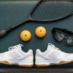 Squash Equipment for Beginners: What You Actually Need (and What to Skip) Photorealistic flat-lay photo of beginner squash equipment: racket, blue-dot balls, court shoes, eyewear on a gym bench