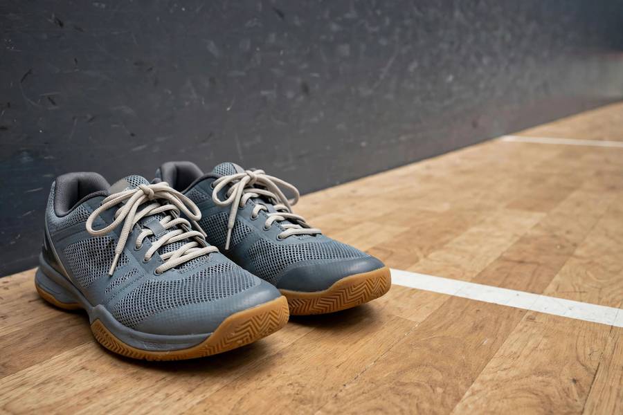 Photorealistic photo of indoor court shoes with non-marking soles beside a squash court floor