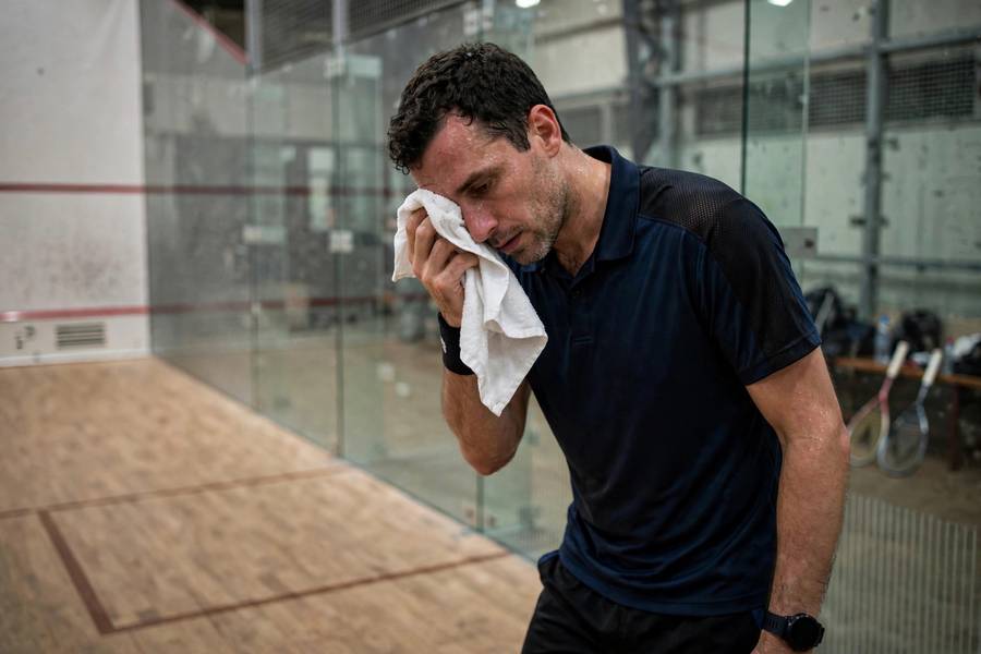 A squash player resting between games with the scoreboard behind