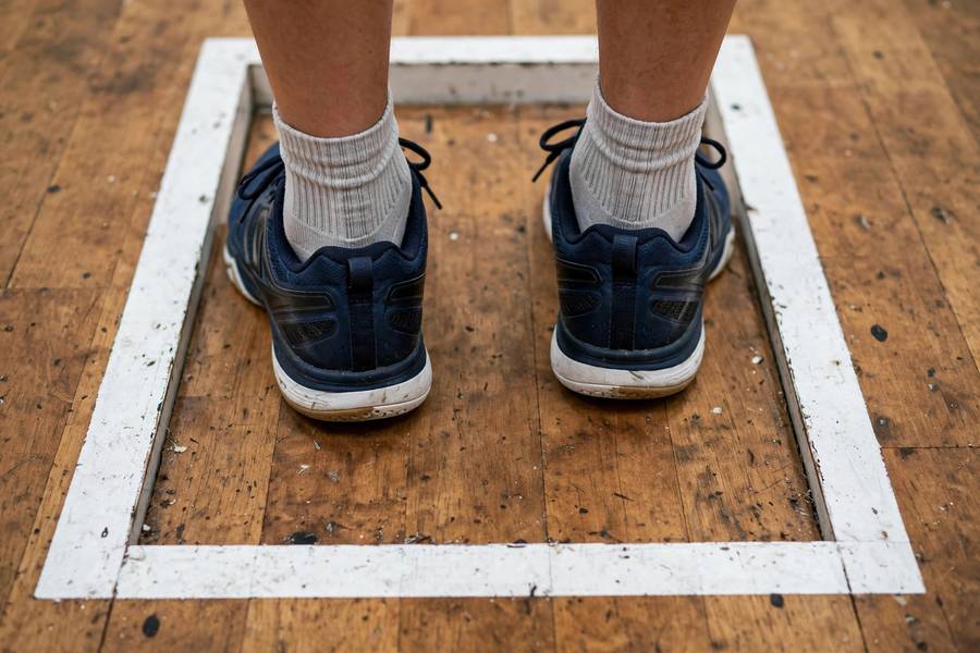 Photorealistic close-up of a player's feet positioned inside the squash service box lines