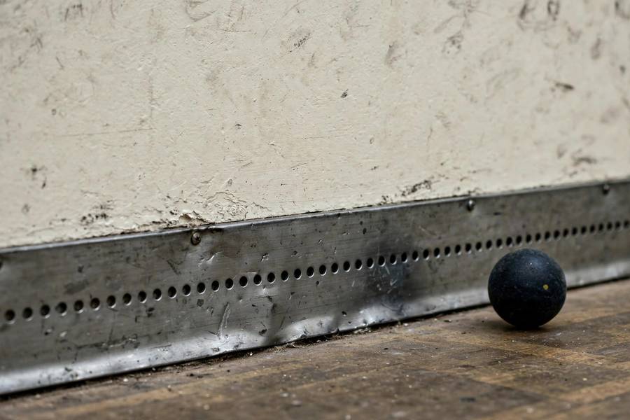 Photorealistic close-up of the metal tin strip along the bottom of a squash front wall, ball nearby
