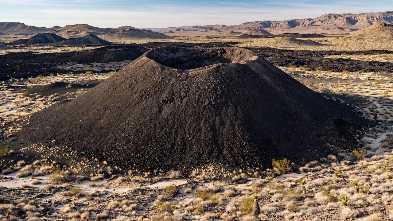 Small cinder cone volcano with a bowl-shaped crater in a desert volcanic field