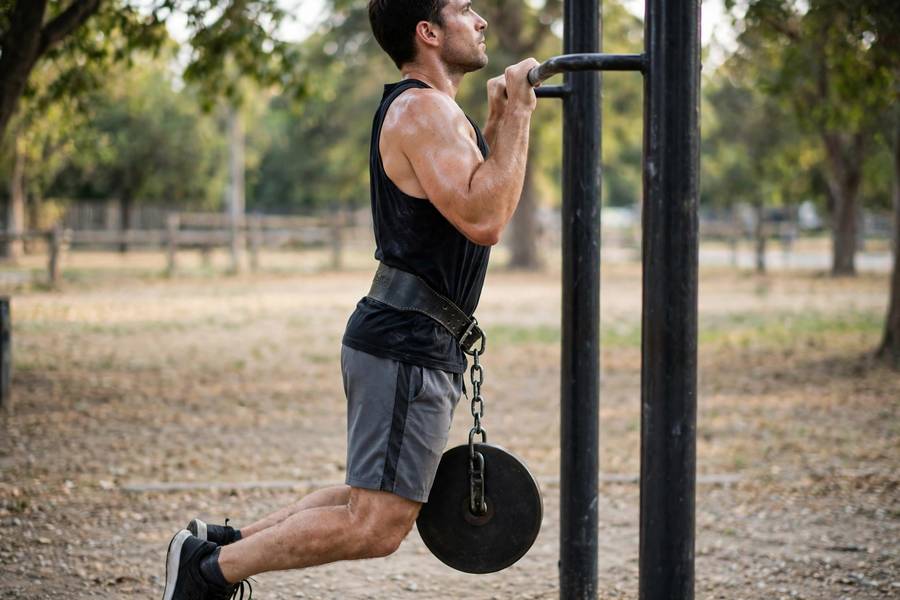 Side view of a man doing a weighted pull-up showing full range of motion