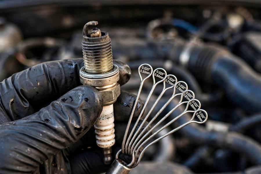 Mechanic inspecting worn spark plug electrodes with a gap gauge