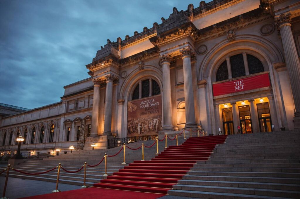 Metropolitan Museum entrance steps with a red carpet at dusk, evening lights glowing