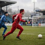 Soccer striker sprinting toward goal with defender chasing, stadium atmosphere