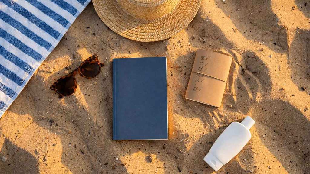 Flat lay of beach vacation essentials with checklist notebook and sunglasses on sand